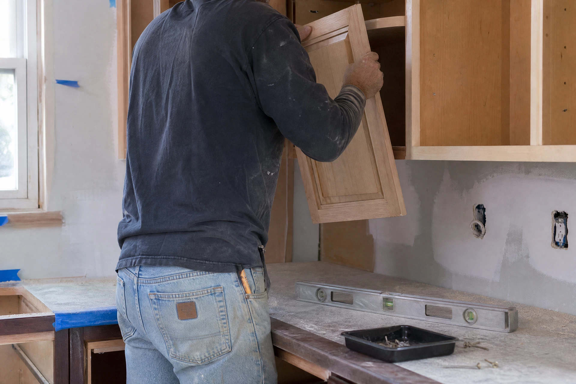 Carpenter aligning a natural wood cabinet door in a partially renovated Idaho kitchen